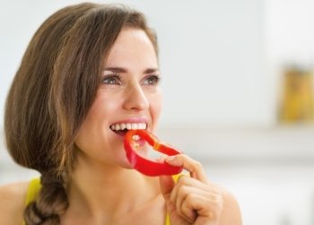 Happy young woman having a bite of red bell pepper