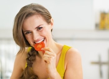 Happy young woman having a bite of red tomato