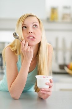 Portrait of thoughtful teenager girl with yogurt in kitchen