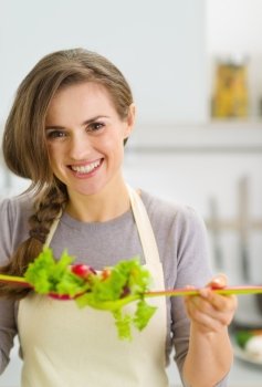 Smiling young housewife mixing fresh salad with spoons