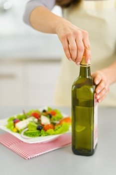 Closeup on woman opening bootle of olive oil to add into salad