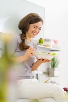 Happy young woman eating fresh salad in modern kitchen