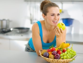 Happy young woman eating apple in modern kitchen