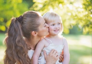 Portrait of mother kissing baby outdoors