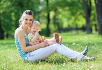Happy mother and baby sitting on grass in park