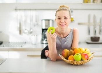 Happy young housewife with apple in modern kitchen