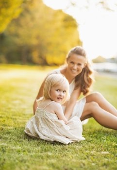 Happy mother and baby sitting on meadow in park
