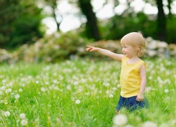 Baby girl on dandelions field pointing on copy space