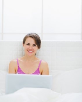 Happy young woman sitting on bed and using laptop