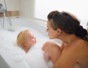 Mother and baby washing in foam filled bathtub