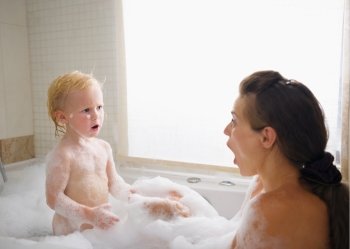 Surprised mother and baby in foam filled bathtub