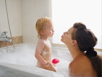 Baby kissing mother while washing in foam filled bathtub