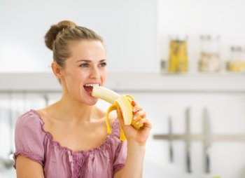 Young woman eating banana in kitchen
