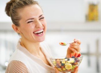 Smiling young housewife eating fruits salad