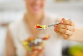 Closeup on young woman giving spoon with fruits salad