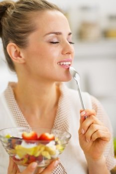 Happy young housewife enjoying fruits salad