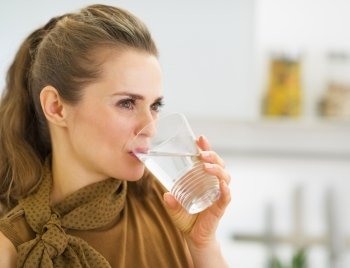 Young housewife drinking water in kitchen