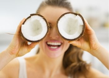 Smiling young woman holding two pieces of coconut in front of eyes