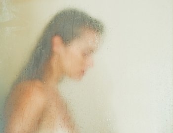 Woman washing behind weeping glass shower door