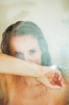 Stressed woman leaning on weeping glass shower door