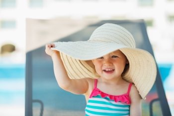 Baby in beach hat sitting on sun bed