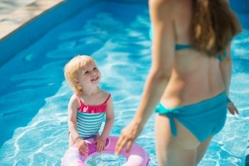 Baby standing in pool with inflatable ring and looking on mother