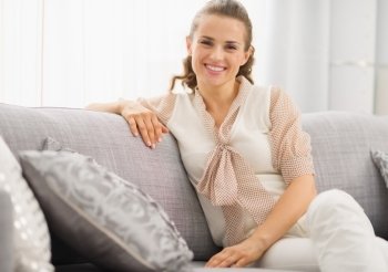 Portrait of smiling young housewife sitting on couch in living room