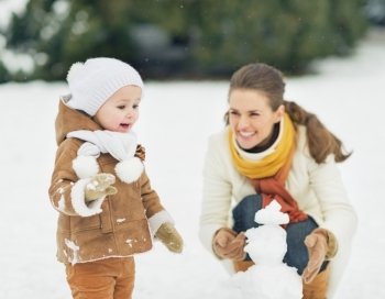 Happy mother and baby making snowman in winter park