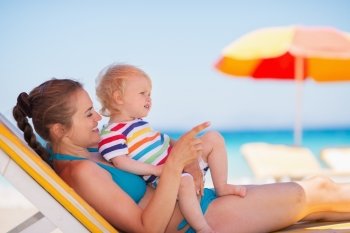 Mother with baby laying on sunbed and pointing on copy space