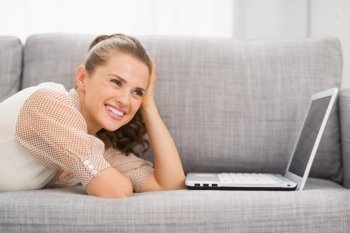 Thoughtful young woman laying on sofa with laptop
