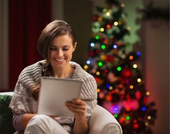 Happy woman looking in tablet PC in front of Christmas tree