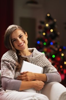 Happy young woman near christmas tree hugging tablet pc