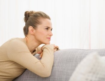 Thoughtful young housewife sitting on sofa looking on copy space