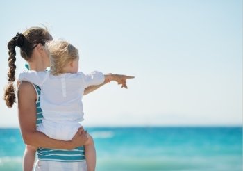 Mother and baby on beach pointing on copy space