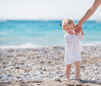 Baby holding mothers hand and walking on beach