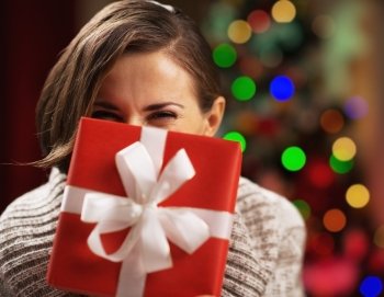 Happy young woman holding christmas present box in front of face