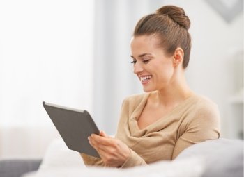 Happy young housewife sitting on sofa and using tablet pc