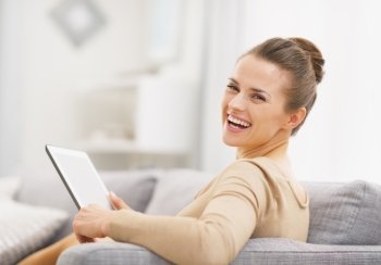 Smiling young woman with tablet pc sitting on sofa