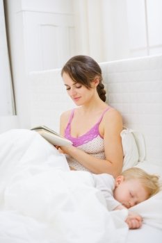 Mother in bedroom reading book while baby sleeping