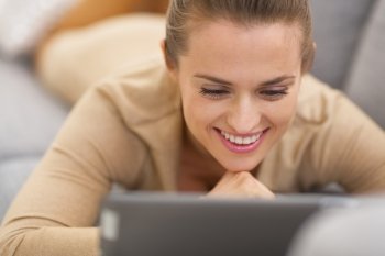 Happy young woman with tablet pc laying on couch