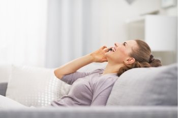Happy young woman talking mobile phone while relaxing on couch