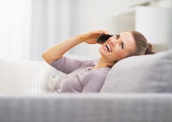 Happy young woman talking cell phone while sitting on couch
