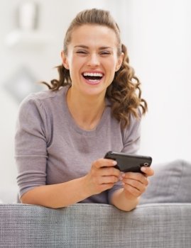 Happy young woman sitting on couch and writing sms
