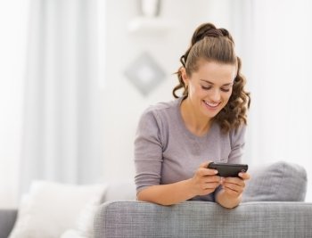 Happy young woman reading sms while sitting on couch