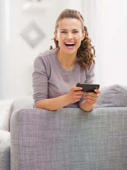 Happy young woman sitting on sofa and writing sms