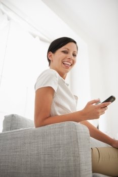 Happy young woman sitting on sofa with mobile phone
