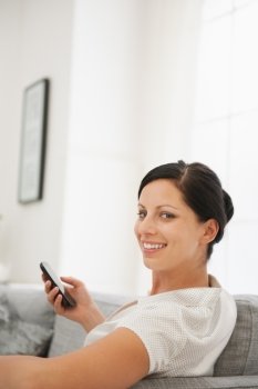 Happy young woman sitting on couch and holding mobile phone