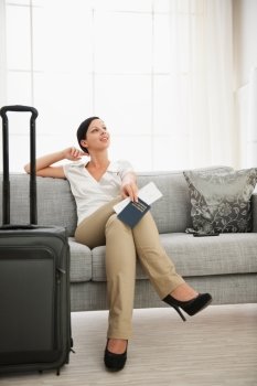 Dreaming woman with passport and air ticket sitting on sofa