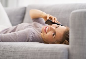 Smiling young woman talking mobile phone while laying on couch