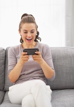 Surprised young woman sitting on sofa and reading sms